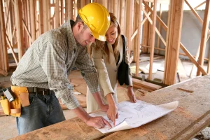 Contractor in a hard hat reviewing blueprints with a client at a framed construction site