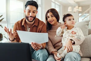 Parents holding a baby review family health plan paperwork together on the couch